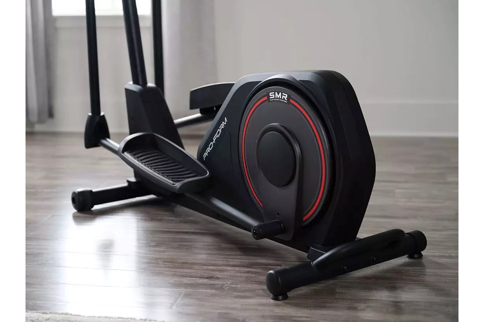 Black and red ProForm Sport elliptical machine with dual handles and foot pedals on wooden floor in home gym setting
