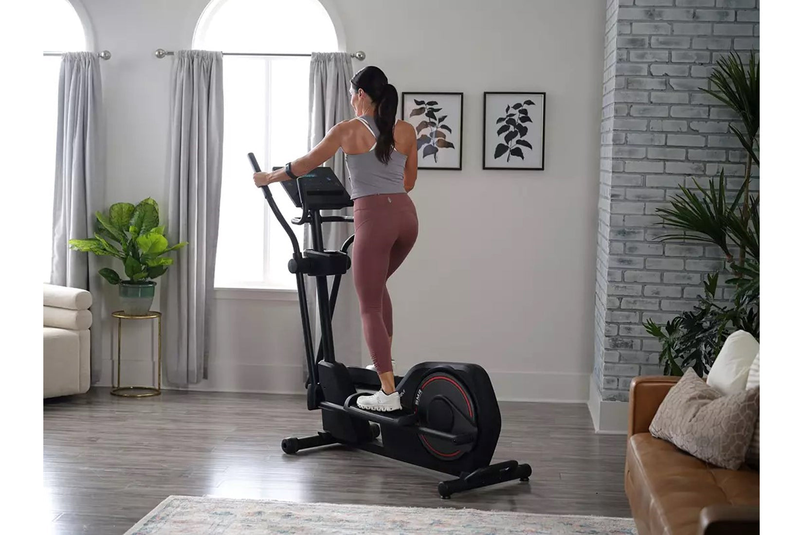 Woman wearing gray tank top and burgundy leggings using black ProForm Sport Elliptical in modern living room setting