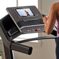 Black ProForm treadmill with digital display showing workout video, control buttons, and red emergency stop button, woman usi