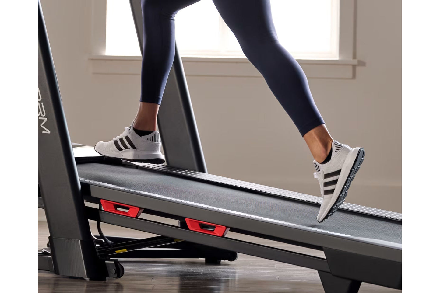Woman wearing navy leggings and white sneakers with black stripes running on ProForm Trainer 1000 treadmill