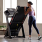 Woman in purple tank top and navy leggings running on black ProForm treadmill with digital display in bright home gym