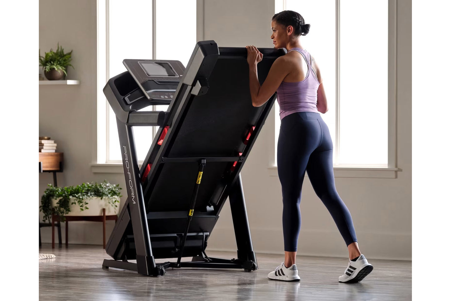 Woman in purple tank top and navy leggings running on black ProForm treadmill with digital display in bright home gym