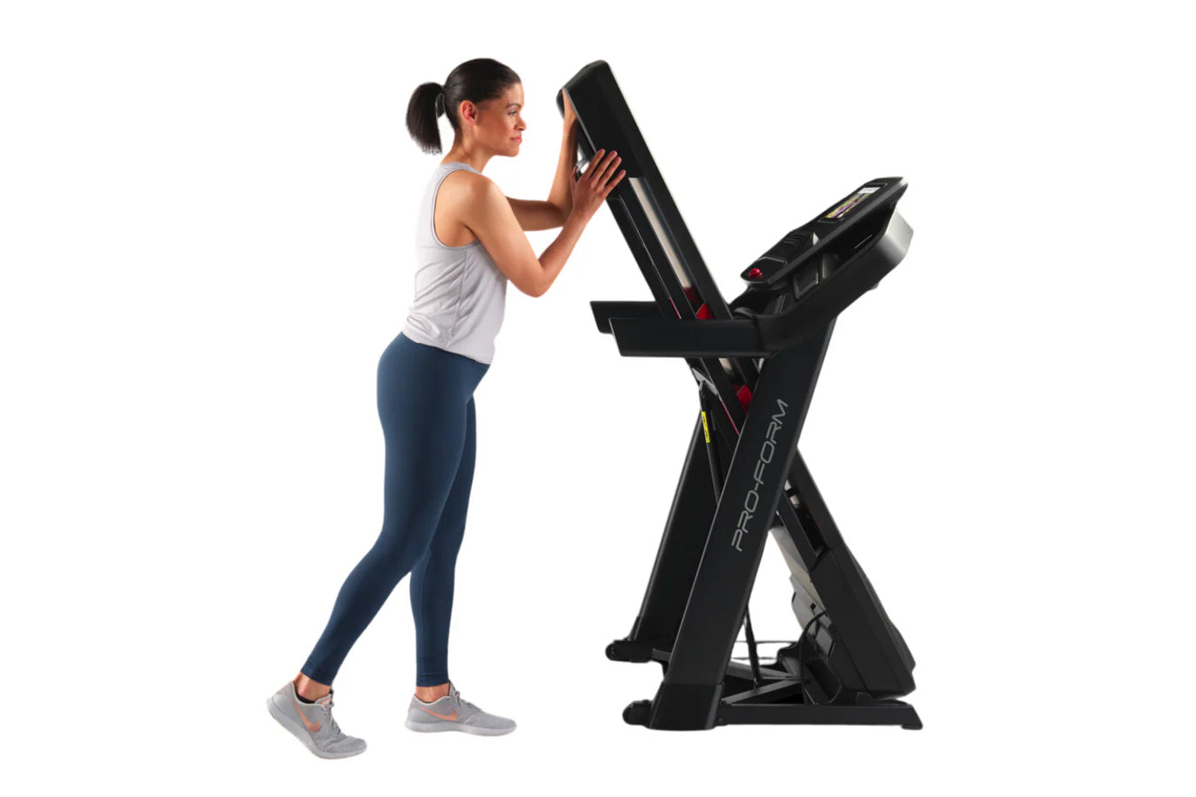 Woman using black ProForm Trainer 1000 treadmill with digital display, wearing white tank top and navy leggings