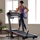 Woman in purple racerback tank and navy leggings running on black ProForm Treadmill with digital display in home gym setting