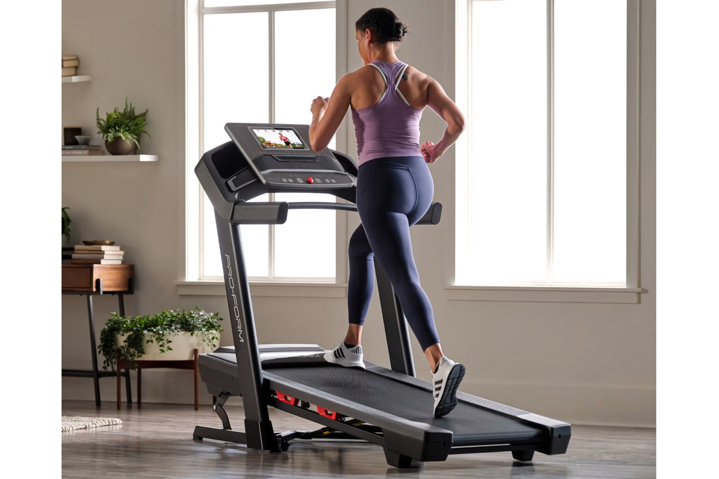 Woman in purple racerback tank and navy leggings running on black ProForm Treadmill with digital display in home gym setting