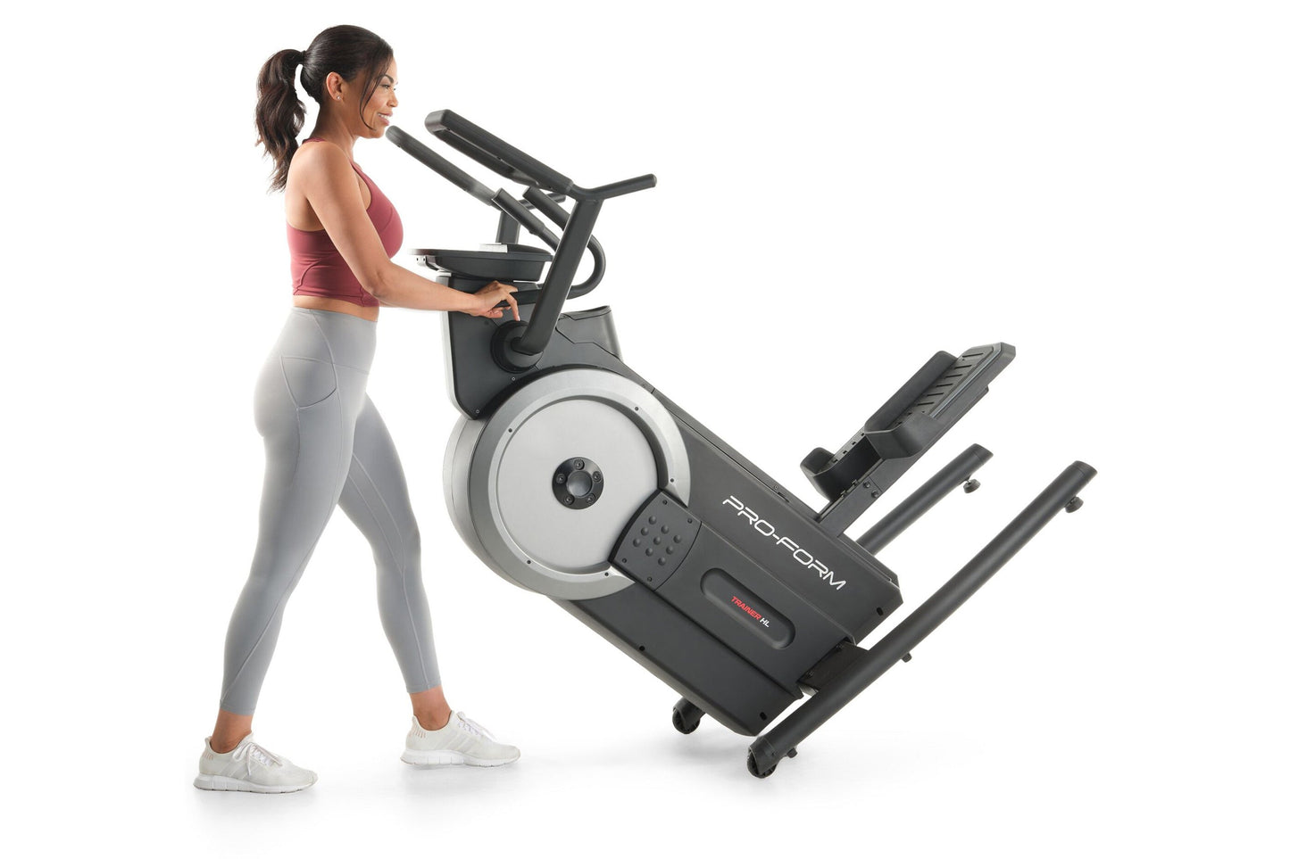 Woman wearing burgundy sports bra and gray leggings using black and gray ProForm elliptical machine with white wheel accent o