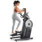 Woman in coral sports bra and gray leggings using black ProForm elliptical trainer with digital display on white background
