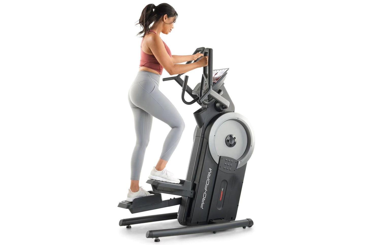 Woman in coral sports bra and gray leggings using black ProForm elliptical trainer with digital display on white background