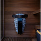 Black metal sauna heater bucket with gray stones, mounted on wooden wall inside sauna