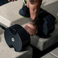 Person in black and neon green athletic shoes lifting black adjustable dumbbell on concrete steps