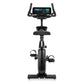 Black upright exercise bike with digital touchscreen console, dual handles, padded seat, and foot pedals with straps on white