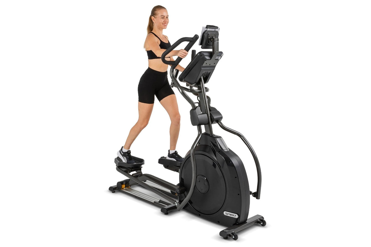 Woman in black sports bra and shorts using black and silver Spirit elliptical machine with digital display on white backgroun