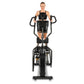 Woman wearing black sports bra on black upright elliptical machine with dual handles against white background