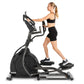 Woman wearing black sports bra and shorts using Spirit XE795 black elliptical machine on white background