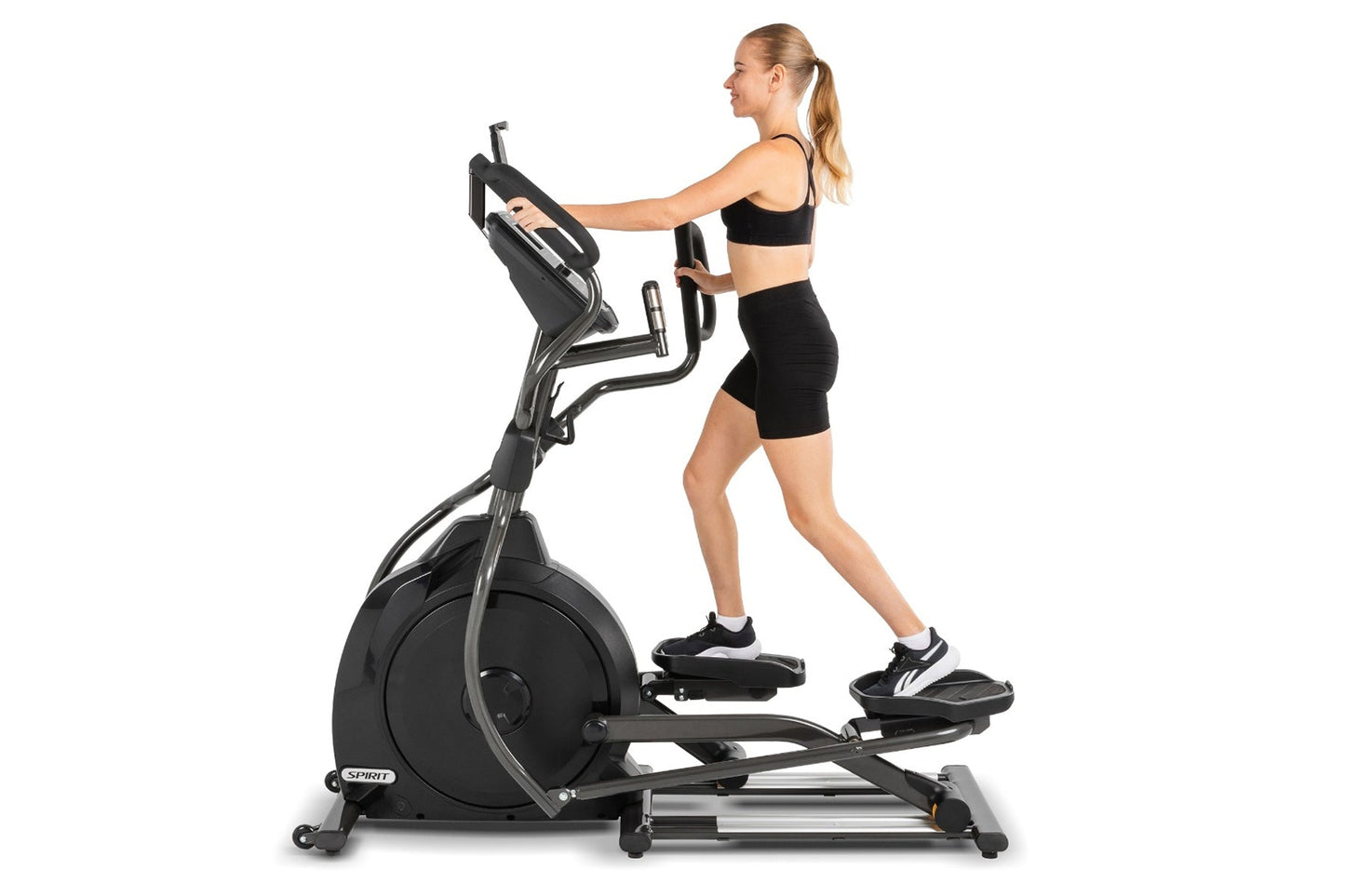 Woman wearing black sports bra and shorts using Spirit XE795 black elliptical machine on white background