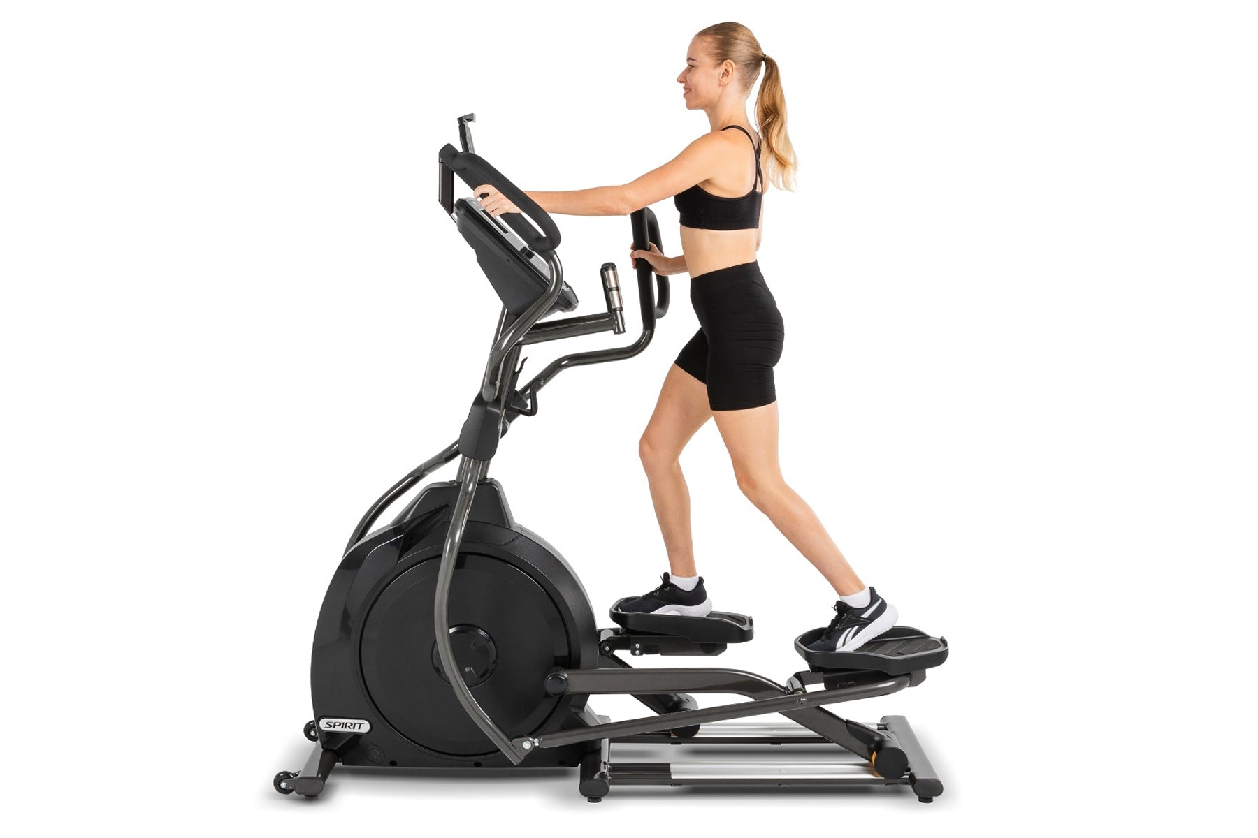 Woman wearing black sports bra and shorts using Spirit XE795 black elliptical machine on white background