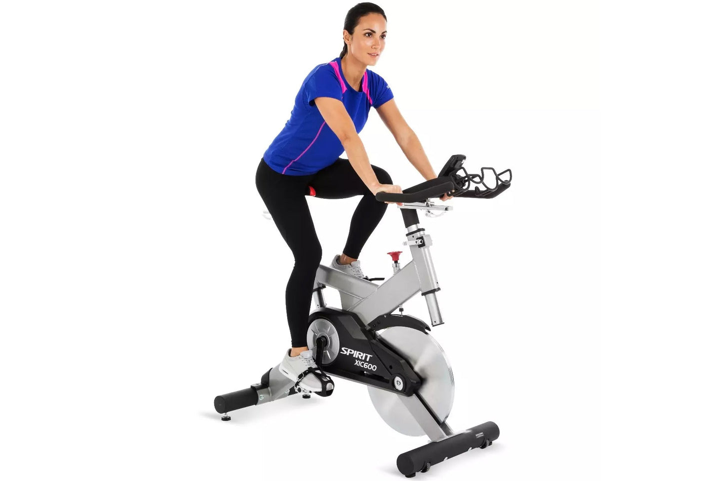 Woman in blue v-neck shirt with magenta trim and black leggings riding Spirit XIC600 stationary exercise bike on white backgr