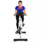 Woman wearing blue and pink athletic top with black leggings, riding white and black stationary indoor exercise bike on white