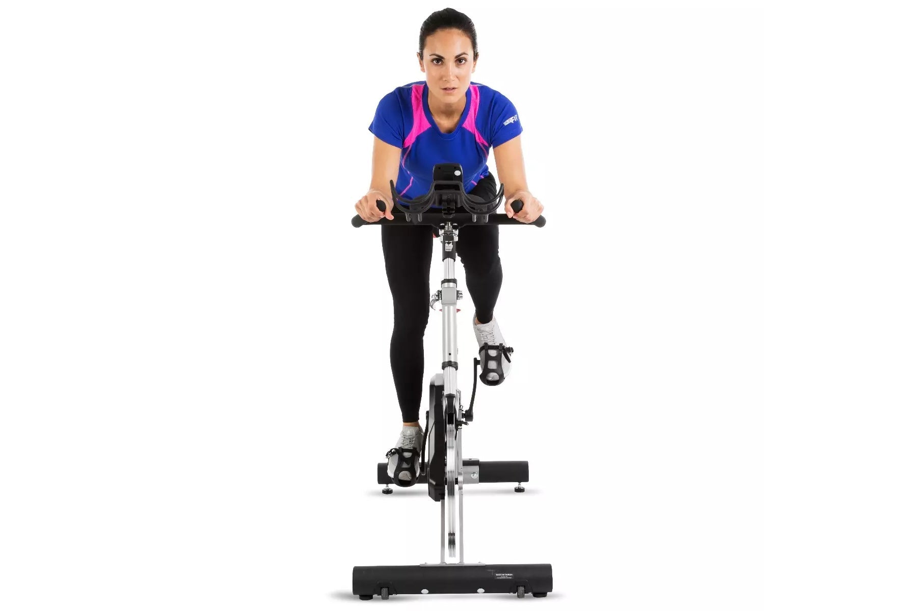 Woman wearing blue and pink athletic top with black leggings, riding white and black stationary indoor exercise bike on white