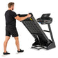 Man in black shirt and shorts running on black Spirit treadmill with digital display, shown from side angle on white backgrou