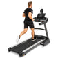 Man jogging on black and silver Spirit XT485 treadmill with digital console display, worn on white background