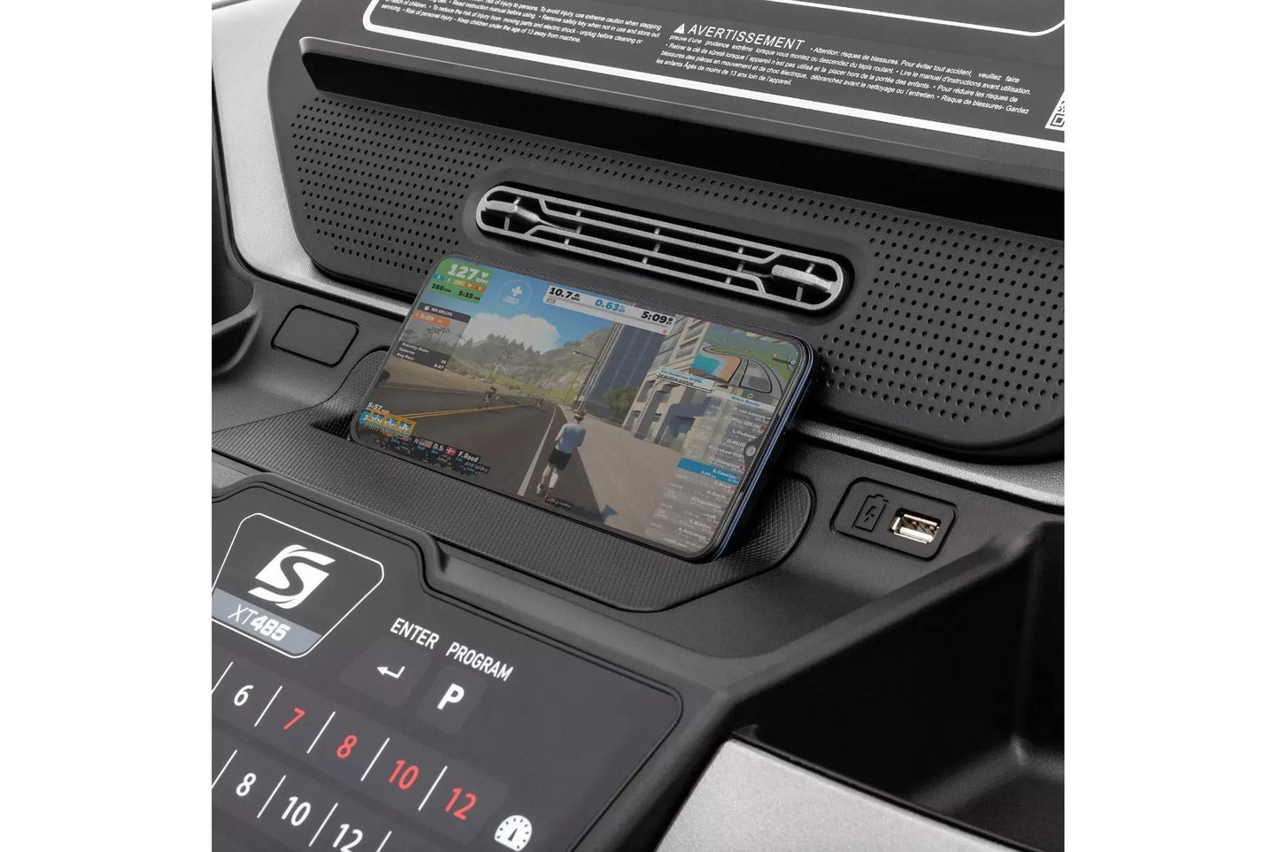 Smartphone displaying racing game on black treadmill console with perforated dashboard and control buttons