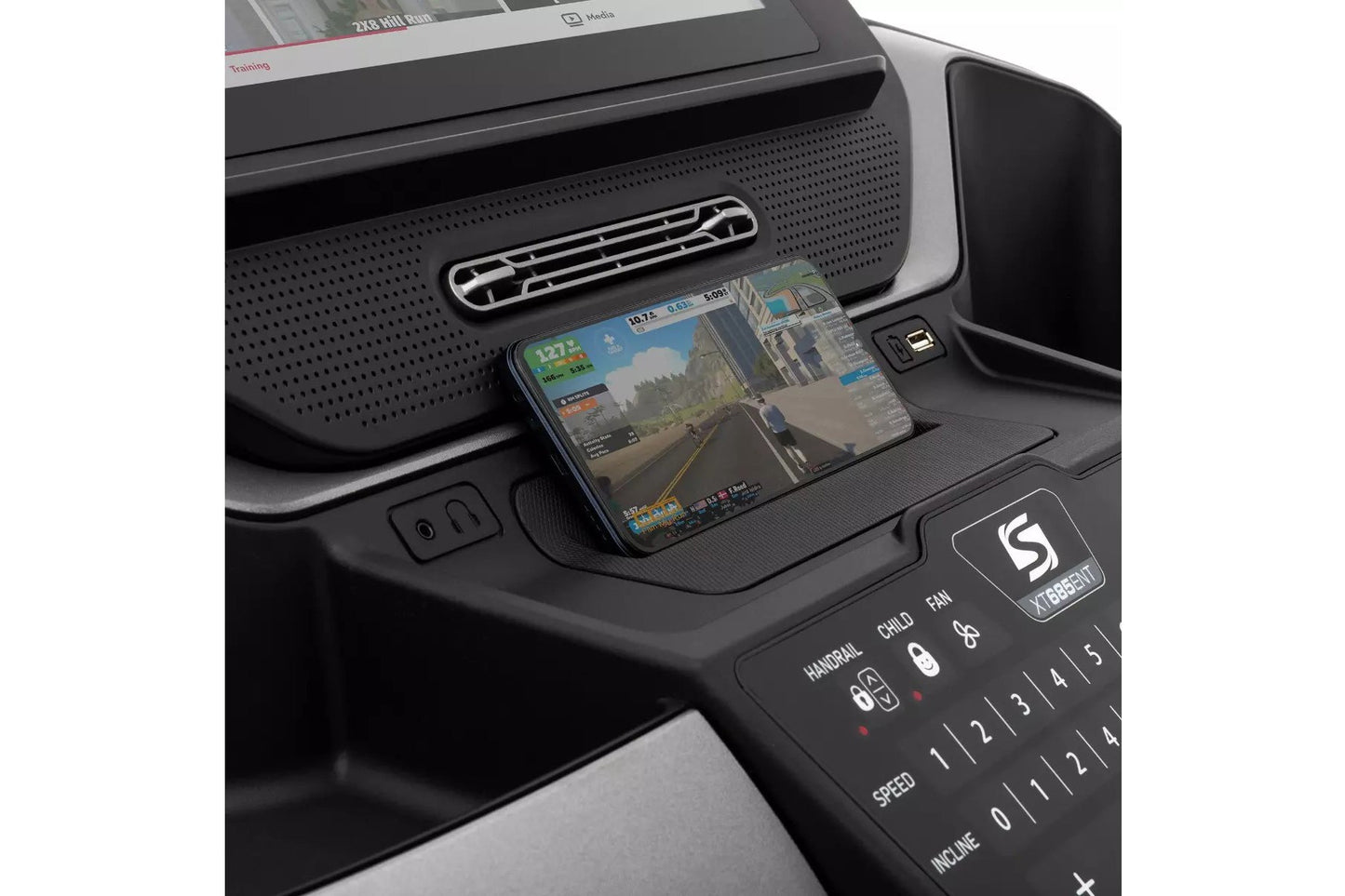 Smartphone displaying racing game mounted on black Spirit XT685ENT treadmill console with control panel visible
