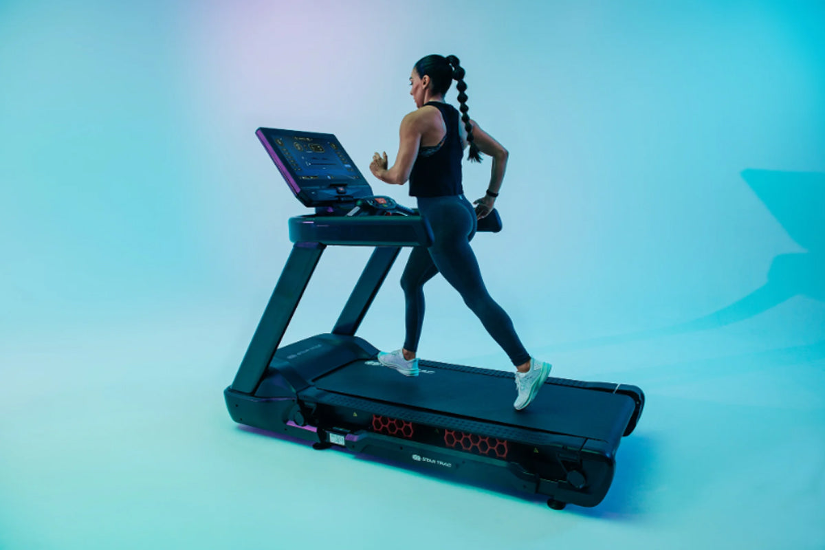 Woman running on black Star Trac treadmill with digital display against turquoise gradient background