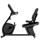 Black recumbent exercise bike with padded seat, digital console, adjustable backrest, and foot pedals on white background