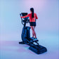 Woman wearing coral long-sleeve top and navy shorts using blue elliptical trainer with digital display against gradient blue 