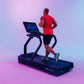 Man jogging on black Star Trac treadmill wearing red sleeveless shirt and black shorts against purple gradient background