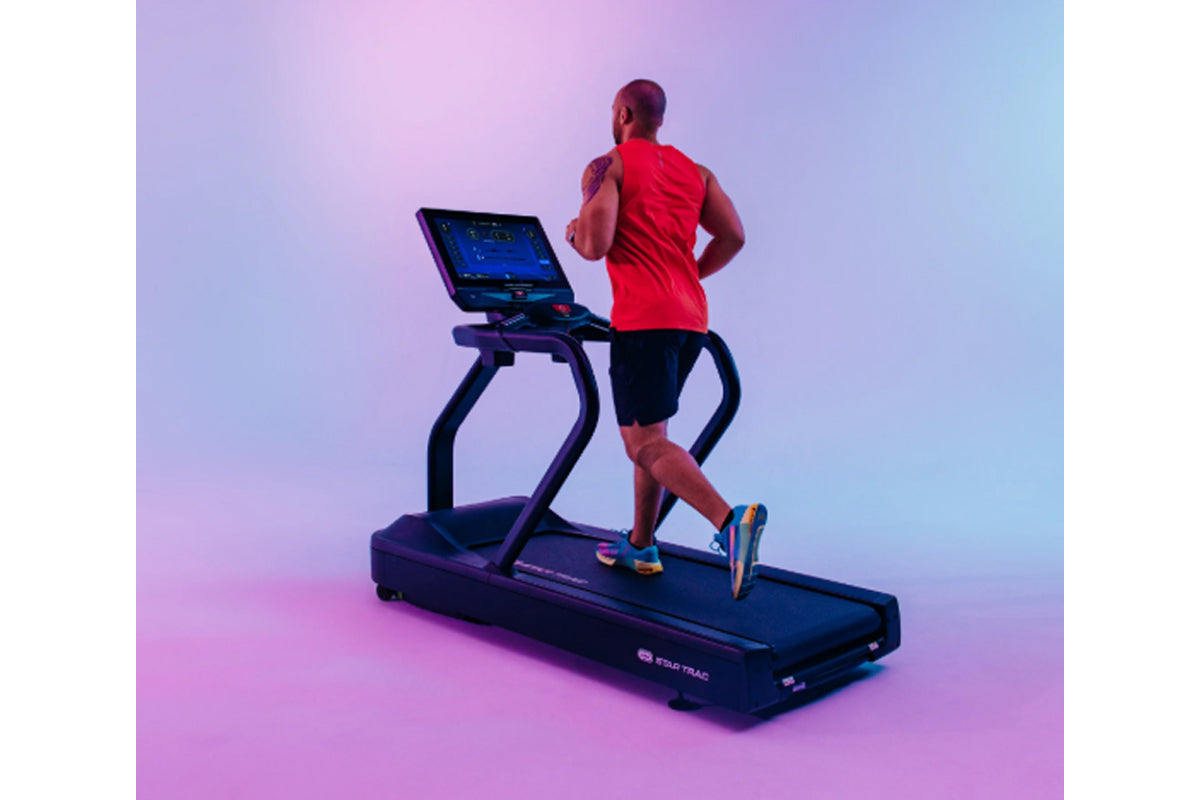 Man jogging on black Star Trac treadmill wearing red sleeveless shirt and black shorts against purple gradient background