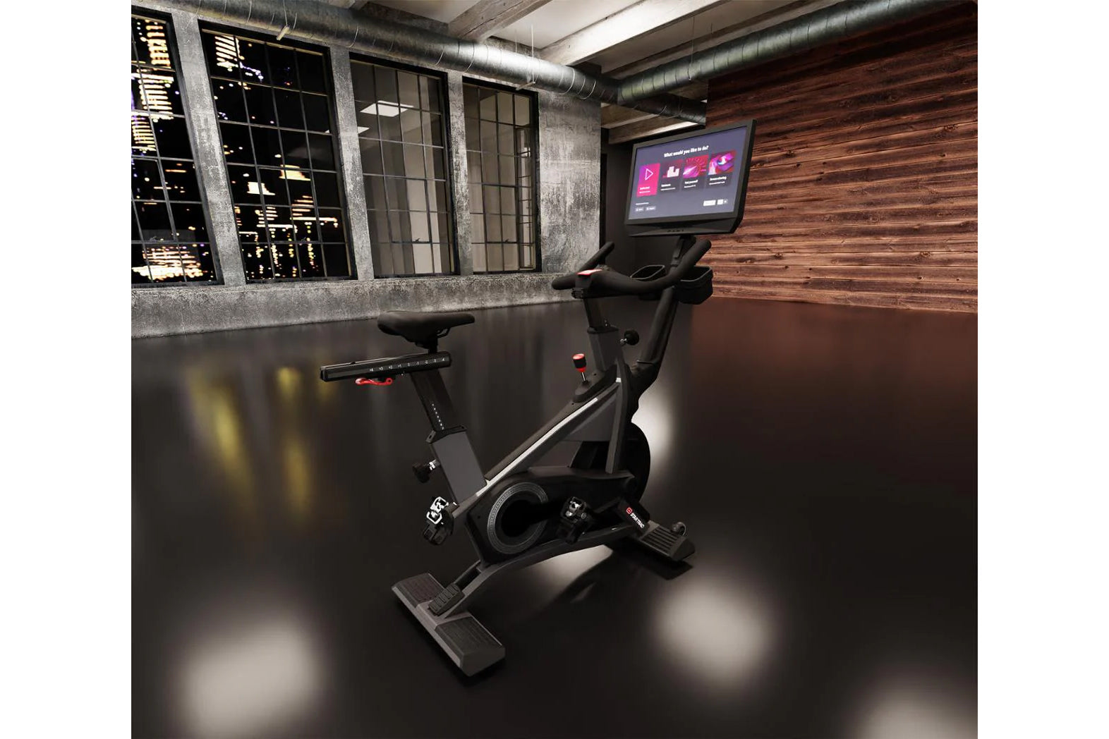 Black stationary exercise bike with digital screen mounted above handlebar, positioned in modern industrial studio setting wi