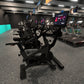 Black stationary exercise bike with digital display in modern gym setting with teal accent wall and equipment visible in back