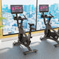 Black stationary exercise bikes with tablet screens in modern gym overlooking city skyline