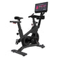 Black stationary exercise bike with digital touchscreen display mounted on upper frame, padded seat, handlebars, and foot ped