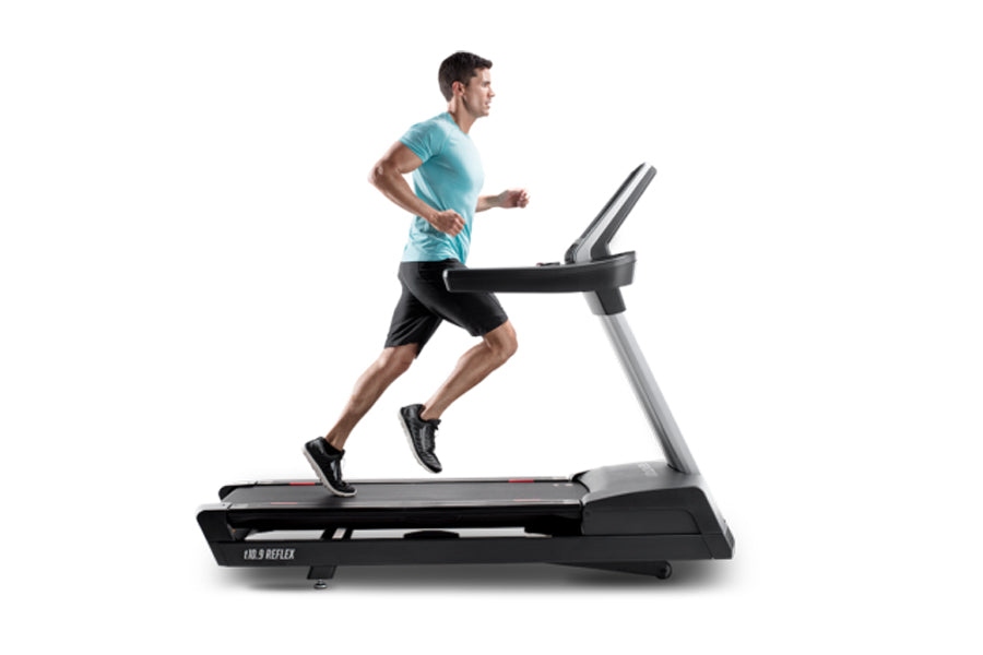 Man in turquoise t-shirt and black shorts running on black and silver treadmill against white background