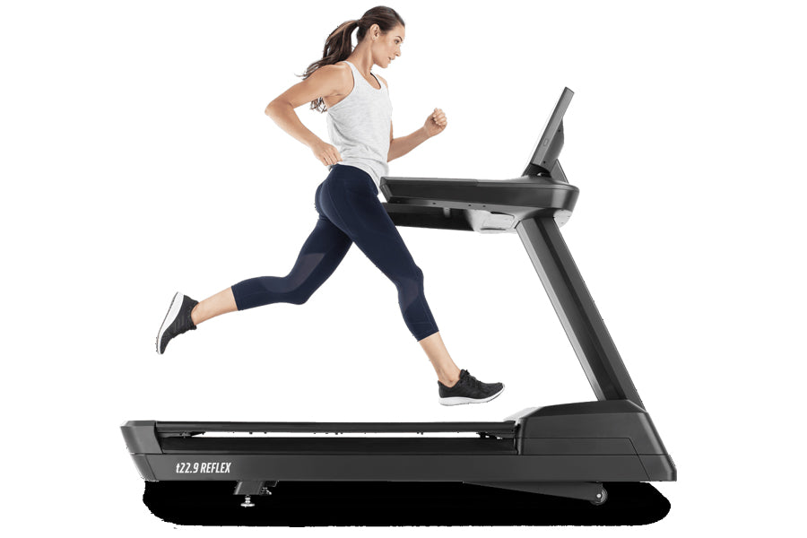 Woman running on black Freemotion t22.9 REFLEX treadmill, wearing white tank top and navy leggings