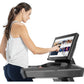 Woman wearing white tank top and navy pants using black treadmill with digital display on white background