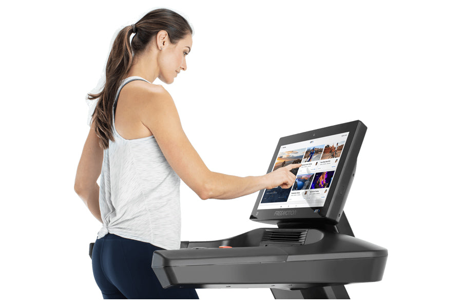 Woman wearing white tank top and navy pants using black treadmill with digital display on white background