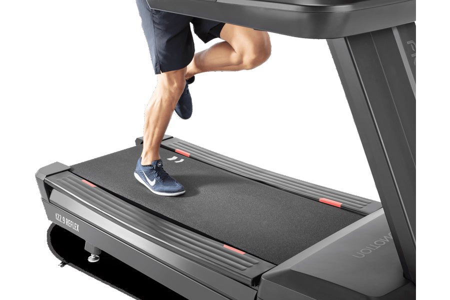 Man running on Freemotion t22.9 REFLEX treadmill with black belt and gray frame, white sneakers visible