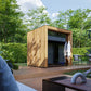Modern wooden cube sauna with dark interior and windows, situated on composite deck surrounded by landscaping and garden furn