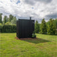 Black vertical wood-slat outdoor sauna with chimney in landscaped garden surrounded by green lawn and evergreen trees