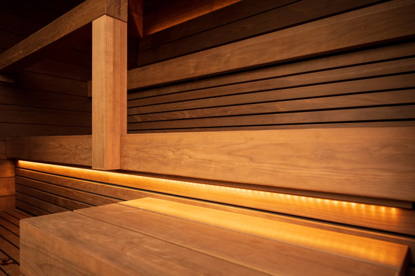 Interior of wooden sauna with horizontal slat walls, vertical post, bench seating, and ambient warm lighting