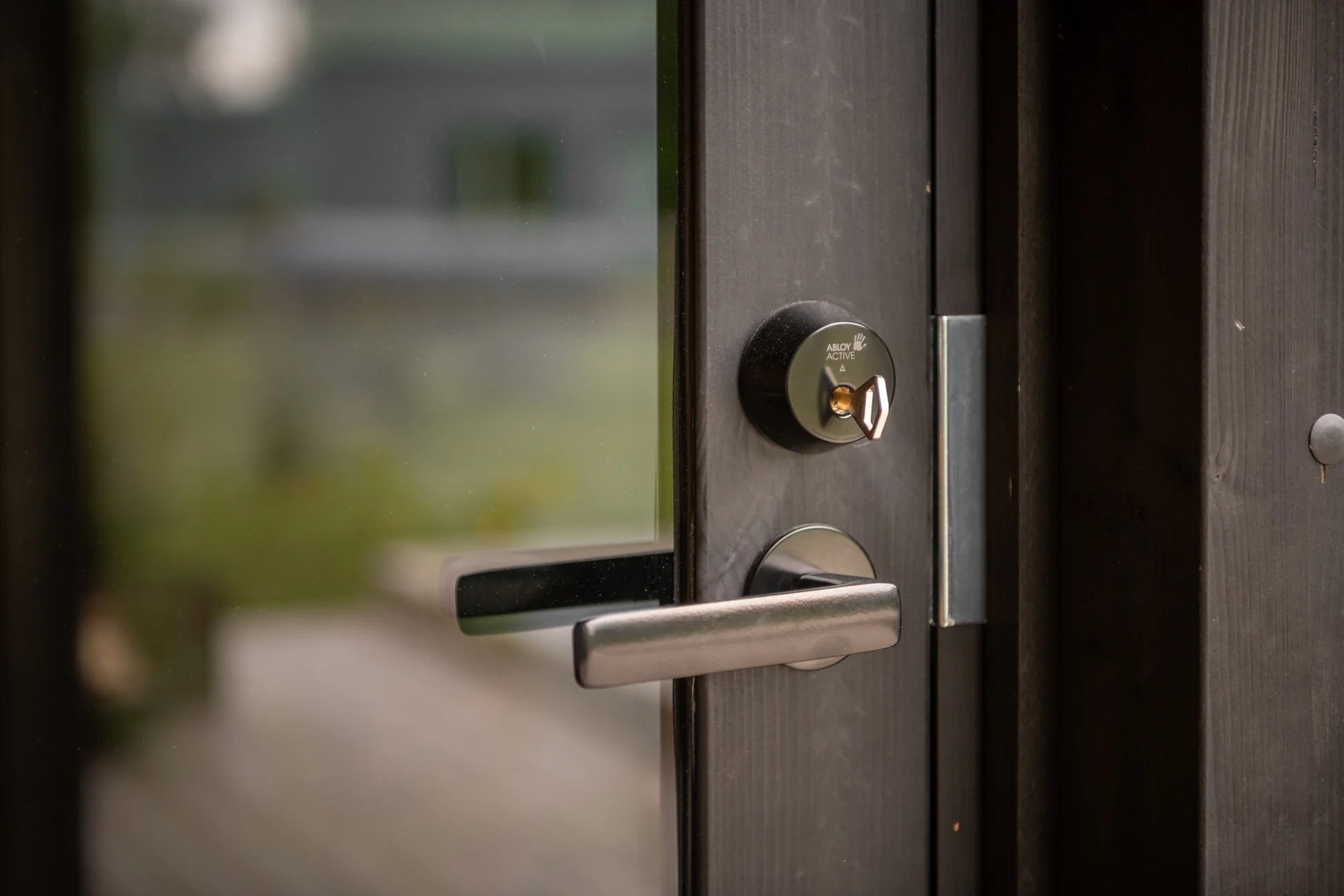 Modern stainless steel door handle and black Abloy Active smart lock on dark wood sauna door
