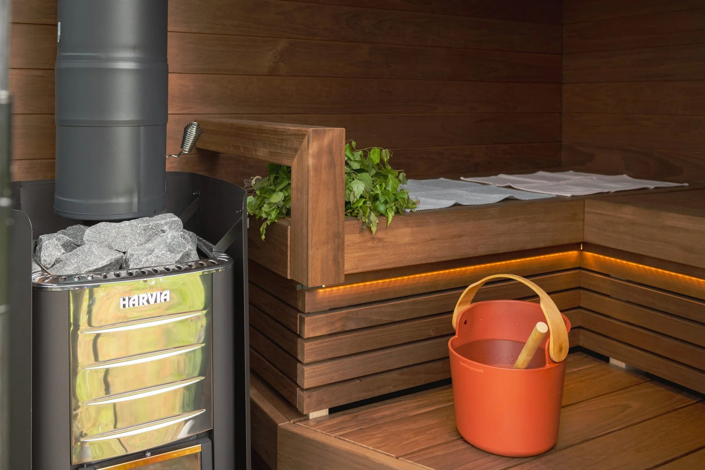 Harvia wood-burning sauna stove with yellow glass front and hot stones inside wooden sauna room with benches and accessories
