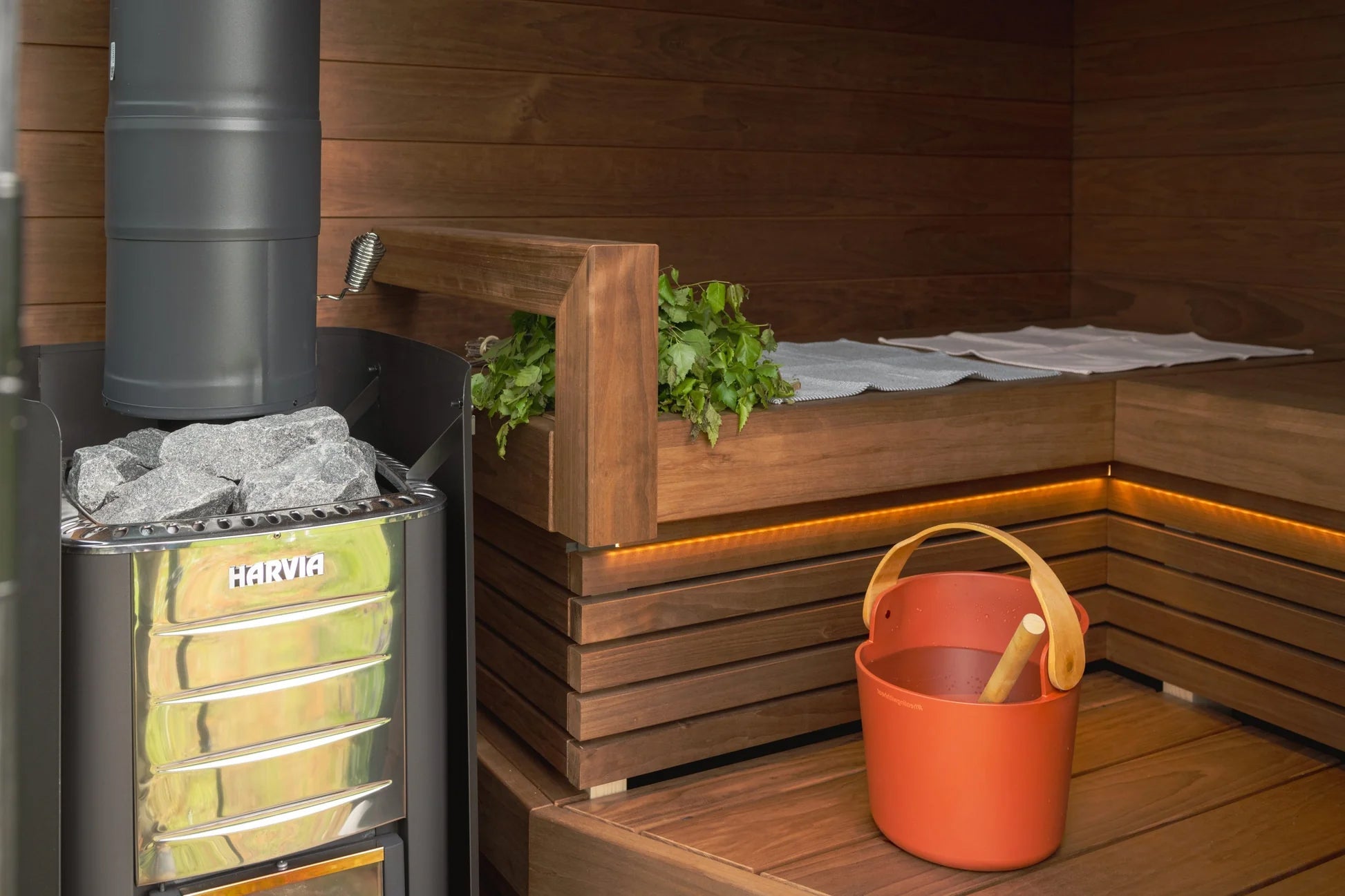 Harvia wood-burning sauna stove with yellow glass front and hot stones inside wooden sauna room with benches and accessories
