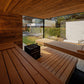 Modern wooden sauna interior with benches, black heater stove, and glass doors opening to outdoor garden patio