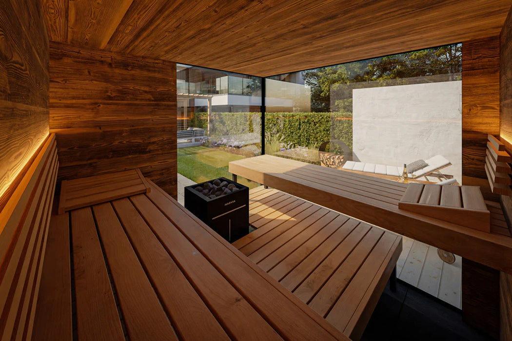 Modern wooden sauna interior with benches, black heater stove, and glass doors opening to outdoor garden patio