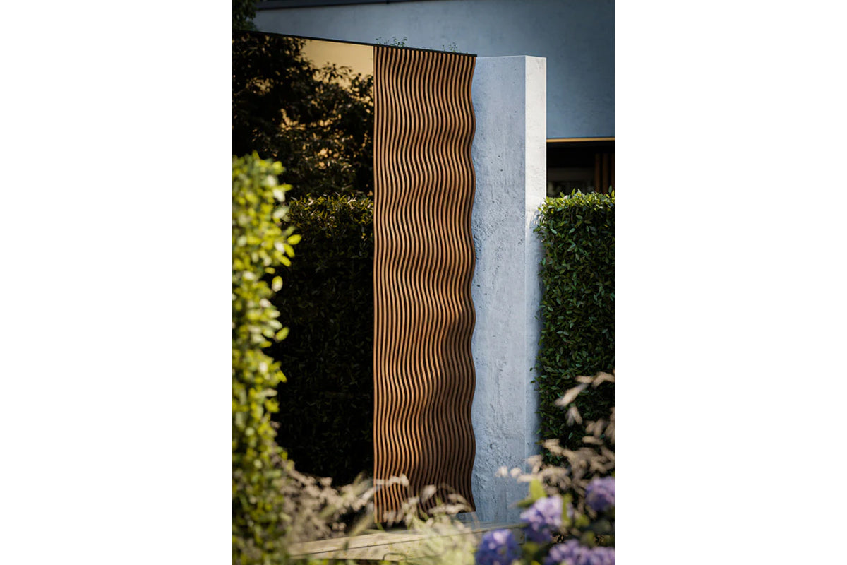 Thermasol Ombra outdoor sauna with vertical wavy wood slats, displayed in garden setting with surrounding greenery and blue b